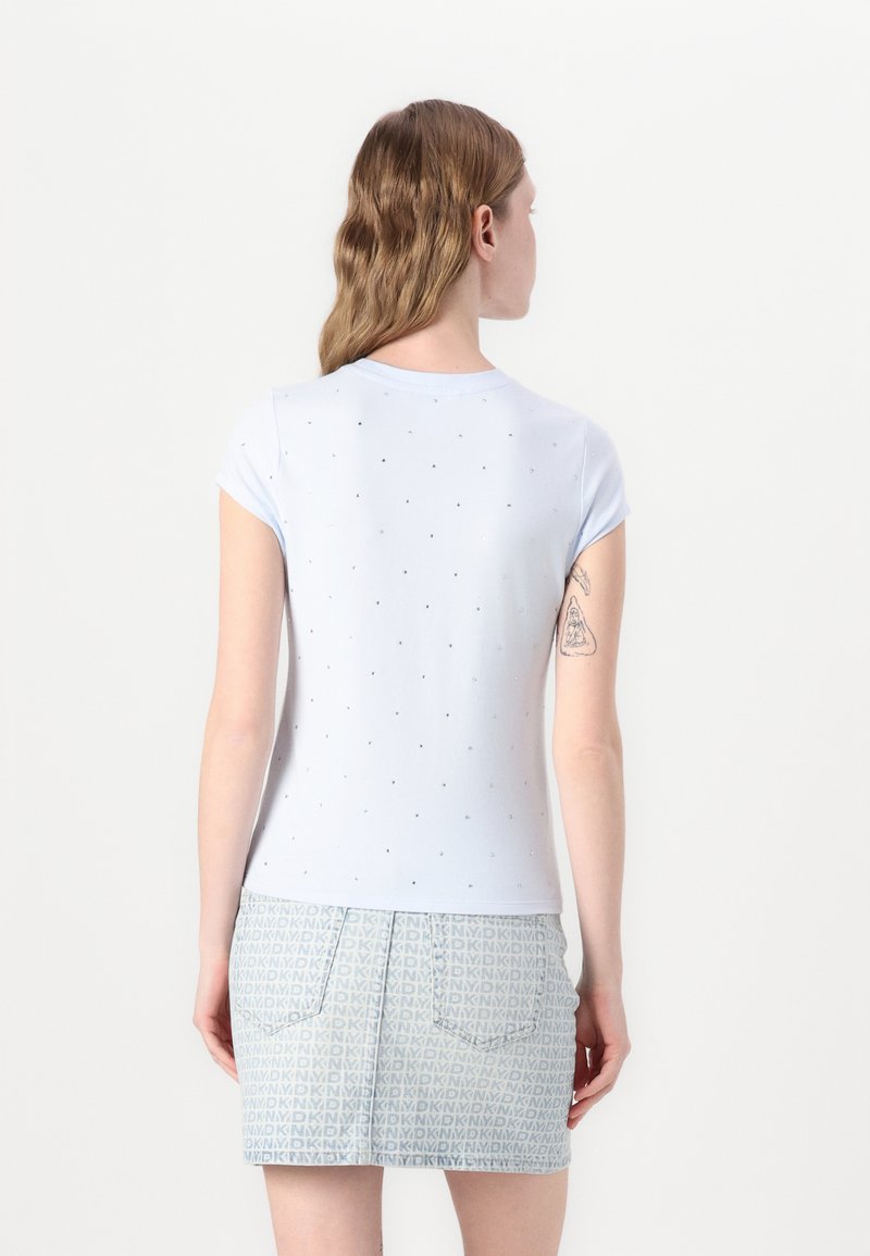 T-shirt azzurro chiaro a maniche corte con piccoli punti argentati lucidi; abbinato a una gonna di jeans con un motivo geometrico blu chiaro e bianco.