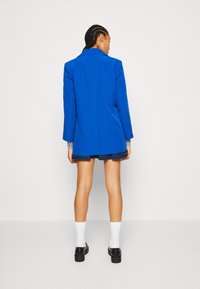 Modra blazer s dolgimi rokavi, prilagojen dizajn, rahla sijaj, v kombinaciji z jeans krilom, belimi nogavicami in debelimi črnimi čevlji.