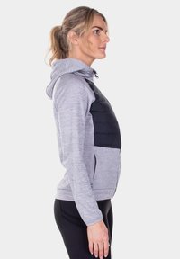 Grijze hoodie met een zwart gewatteerd voorpaneel, voorzien van een ritssluiting, zijzakken en een capuchon met trekkoord. Zachte textuur overal.