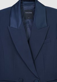 Blazer bleu marine avec des revers en satin, fermeture à double bouton et une poche poitrine, étiqueté taille petit par la marque Calliope.