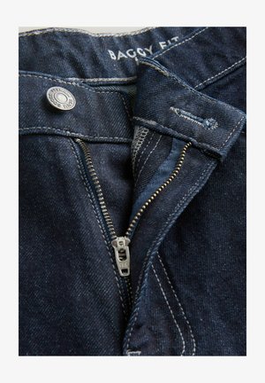 Dunkelblaue, weit geschnittene Jeans mit einem Metallreißverschluss, sichtbaren Nähten und einem markierten Knopf am Bund. Die Textur wirkt wie Denim.