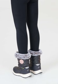 Sorte vinterstøvler med grå faux pels i kanten, quiltet tekstur og lyserødt emblem på en glat overflade. Sammen med sorte leggings.