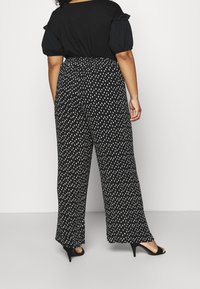 Černý top s nafouklými rukávy, kombinovaný s černými kalhotami s vysokým pasem, které mají bílý puntíkovaný vzor. Na modelce černé sandály na podpatku.