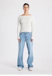 White, textured long-sleeve top with a boat neckline, paired with light blue wide-leg jeans and white sneakers. Simple design with gathered fabric.