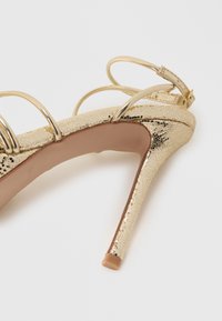 Sandale aurii cu toc înalt, având un model texturat de piele de șarpe, cu bretele subțiri, cataramă la gleznă și toc stiletto elegant.