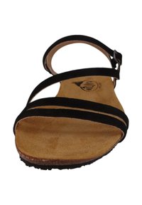 Sandalia de ante negro con tres correas delgadas, hebilla ajustable en el tobillo y plantilla de cuero natural; suela plana con ligera textura.