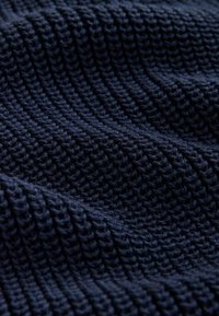 Tissu tricoté bleu foncé avec un motif côtelé texturé, montré en gros plan avec des détails visibles du tissage.