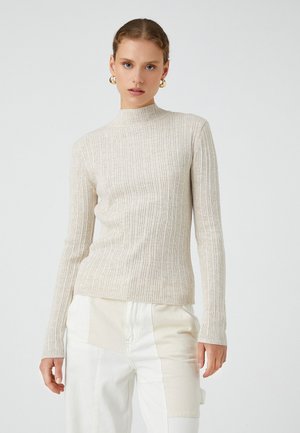 Ljust beige ribbade stickade polotröja med långa ärmar, som har en figurnära silhuett och subtil textur. Matchad med ljusa byxor.
