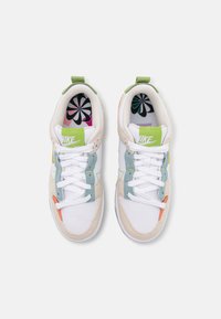 Vita och beige sportskor med gröna, orangea och blå accenter. Har en texturerad yta och vadderad plös med en färgglad inredningsdesign.