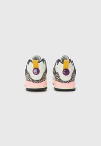 Vista trasera de zapatillas que presentan cuero blanco, acentos negros, entresuela rosa y un talón amarillo con detalle de logo morado y patrón texturizado.