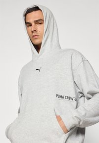 Siva dukserica od mekanog pamuka s vezicom na kapuljači, prednjim džepom, crnim Puma logom i natpisom "PUMA CREW '43".