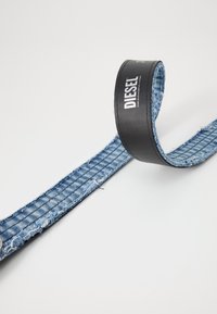 Denim belte med en mørk lærsløyfe, utstyrt med en tydelig logo. Beltet er blått med et teksturert mønster og oppflisede kanter.