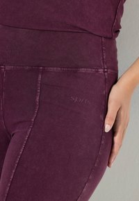 Leggings color bordeaux realizzati in un tessuto misto cotone elasticizzato, con una fascia alta in vita e un discreto dettaglio con logo "sports" sul lato.