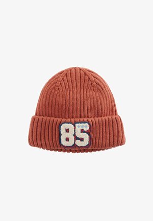 Strickmütze in Rostfarbe, mit geripptem Design und umgeschlagenem Saum, versehen mit einem weißen und blauen gestickten Patch mit der Nummer '85'.