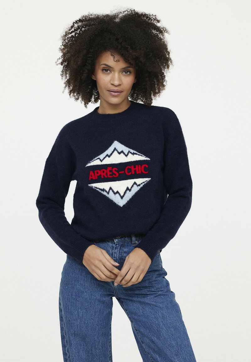 Marineblauer Strickpullover mit einem weißen und roten Berggrafik und dem Text "APRES-CHIC". Der Rundhalsausschnitt und die gerippten Bündchen ergänzen das Design.