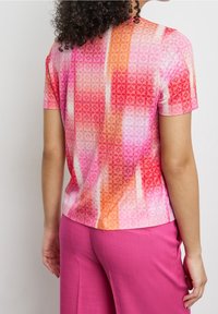 Top de manga corta con un vibrante patrón geométrico en rosa, naranja y blanco. Tejido suave con un corte relajado, combinado con pantalones rosas.