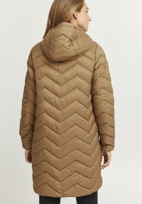 Brun isoleret pufferjakke med hætte, der har et chevronmønster, lange ærmer og en knælængde. Glat tekstur, praktisk design.