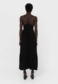 Robe maxi noire avec un corsage ajusté et une jupe à volants. Présente des fines bretelles croisées à l'arrière et une fermeture à nouer dans le dos. Texture lisse.
