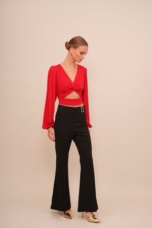 Red long-sleeve top with a twist front and cutout, paired with high-waisted black flared pants and gold high heels. Minimalist design.