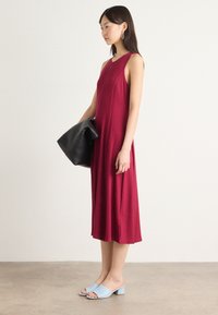 Viininpunainen hihaton mekko, jossa on pystysaumat ja virtaava siluetti, yhdistettynä vaaleansinisiin avokkaisiin, joissa on paksu korko, ja mustaan laukkuun.