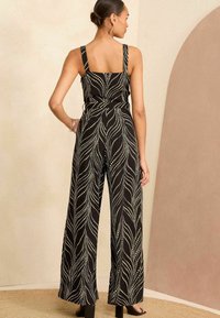 Fekete overál széles lábakkal, fehér pöttyökből készült levélmintával. Állítható pántok és négyzet alakú hátkivágás jellemzi. Simább szövet textúra.