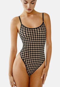 Svart och beige hounds-tooth mönstrad baddräkt med tunna band, rundad halsringning och höga benöppningar. Mjukt, texturerat tyg.