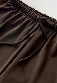 Braune Sportshorts mit einem elastischen Bund und Kordelzug. Das Material wirkt glatt und dehnbar, ideal für Komfort und Bewegungsfreiheit.