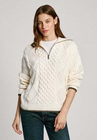 Kreminės spalvos megztinis su kabelių ir deimantų raštais, turintis užtrauktuko apykaktę ir kantą su žaliais akcentais.