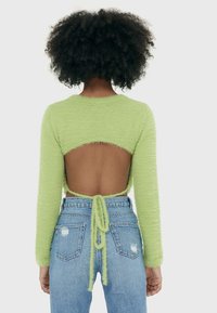 Un haut vert duveteux à manches longues avec une découpe dans le dos, noué à la taille, associé à un jean en denim bleu taille haute avec des détails déchirés.