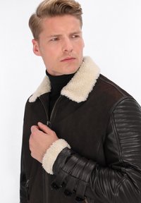 Jachetă din piele maro, cu un guler și manșete din blană sintetică crem, având detalii din piele cu textură ribbed pe mâneci și închidere cu fermoar frontal.