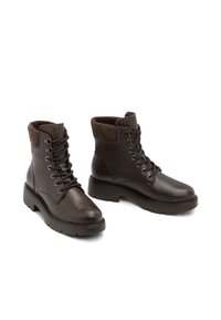 Botas de tobillo de cuero marrón con un acabado suave, suela plana resistente, cordones en la parte delantera y un suave puño de tela marrón en la parte superior.