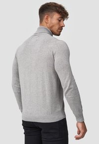 Pull en tricot gris avec un col montant, des manches longues, et des bords côtes au niveau des poignets et de l'ourlet, porté par un mannequin vu de dos.