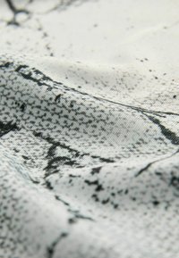 Tekstūruotas audinys, rodantis juodai baltą abstraktų raštą, turintis įvairių formų ir taškų, su lygiu paviršiumi ir nežymiu blizgesiu.