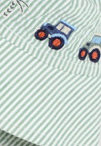 Green and white striped fabric featuring embroidered blue and gray tractors with orange wheels. Soft texture, casual design.