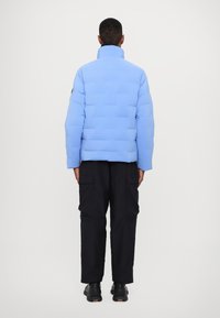 Light blue padded jacket with a high collar, featuring a geometric pattern. Paired with black cargo pants and black shoes.