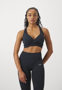 Sujetador deportivo oscuro con diseño envolvente y tirantes anchos, combinado con leggings oscuros de tiro alto que cuentan con un logo. Tela suave y elástica.