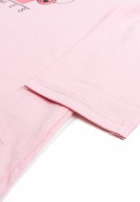 Primo piano dell'orlo e della manica di una maglietta di cotone rosa chiaro con cuciture visibili e parte di un design stampato.