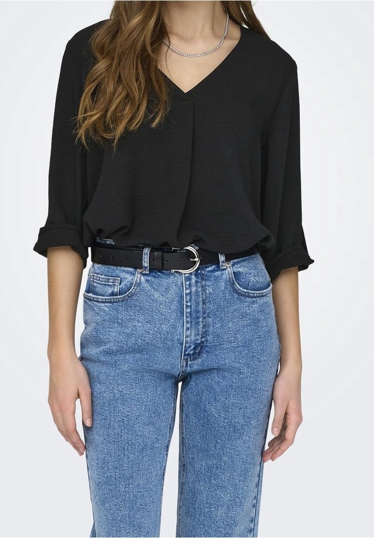 Black, V-neck top with rolled sleeves, paired with high-waisted blue denim jeans featuring front pockets and a black belt with silver hardware.