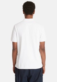 Bílá polo košile s klasickým límcem a krátkými rukávy, vyrobená z měkké bavlněné tkaniny. Pohled z pohledu zezadu ukazuje minimální detaily.