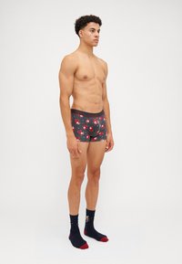 Herren Boxer Shorts in Dunkelgrau mit rotem und weißem Weihnachtsmann-Gesichtdruck. Schwarzen Bund mit grauem Logo. Strukturierter Stoff, enganliegende Passform. Schwarze und rote Socken.