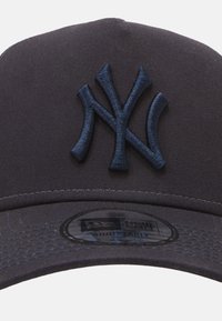 Cappellino da baseball blu scuro con logo NY ricamato in rilievo. Presenta una visiera piatta e una fascia regolabile con etichetta interna brandizzata. Tessuto dalla superficie liscia.