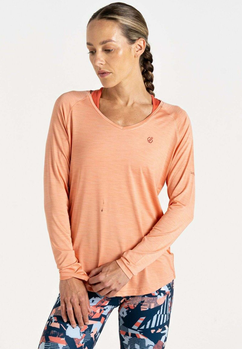 Langärmliges V-Ausschnitt-Oberteil in hellkorallenfarbend mit einer subtilen Textur. Kombiniert mit gemusterten Leggings mit geometrischen Designs in Blau, Orange und Weiß.