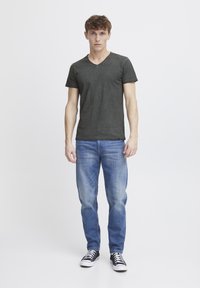 Grå v-hals t-shirt med korte ærmer, parret med lyseblå jeans og sorte sneakers. Enkelt design og afslappet pasform med en glat tekstur.