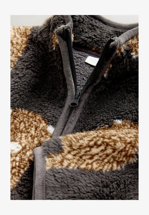 Chaqueta de felpa con cremallera en gris y marrón, fabricada en material suave. Presenta una cremallera negra y diferentes texturas con patrones moteados.