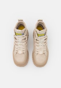 Baskets montantes beiges en suede, avec une semelle en caoutchouc texturé et une étiquette de langue ornée de motifs. Elles comportent des lacets contrastants et des accents de marquage.