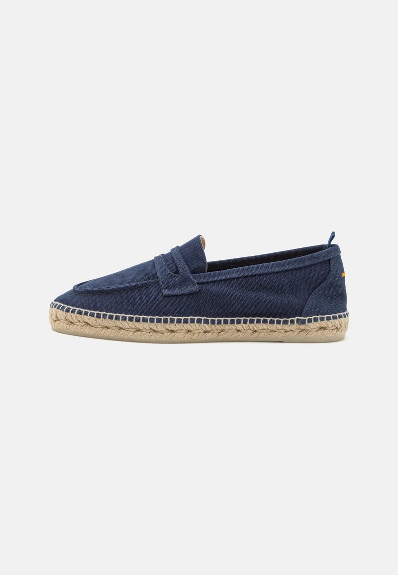 Zapato de lona azul marino tipo slip-on con suela de yute, que presenta una punta alargada y recta, y un acento decorativo de costura a lo largo del borde.