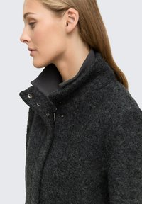 Veste en laine grise avec un col haut, fermeture à pression et à zip, tissu texturé et design moderne et sportif. Aucune motif ni accent visible.