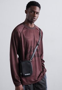 Maroon long-sleeve shirt with black accents, features a round neck and raglan sleeves. Includes a small black crossbody bag with white text.