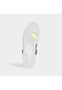 Vit gummiyttersula med cirkulära greppmönster och en grön accent. Ovandelen har en blandning av svarta och ljusa material.