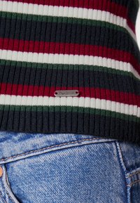 Maglione a righe lavorato a maglia con linee orizzontali rosse, bianche, verdi e blu navy, caratterizzato da una texture a costine e un'etichetta metallica del marchio.